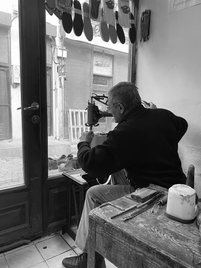 Elderly shoemaker crafts shoes in a quaint workshop, showcasing artisan skills.