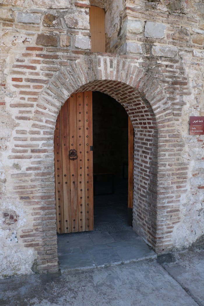 Explore this historic arched doorway featuring a wooden door set within a stone building facade.